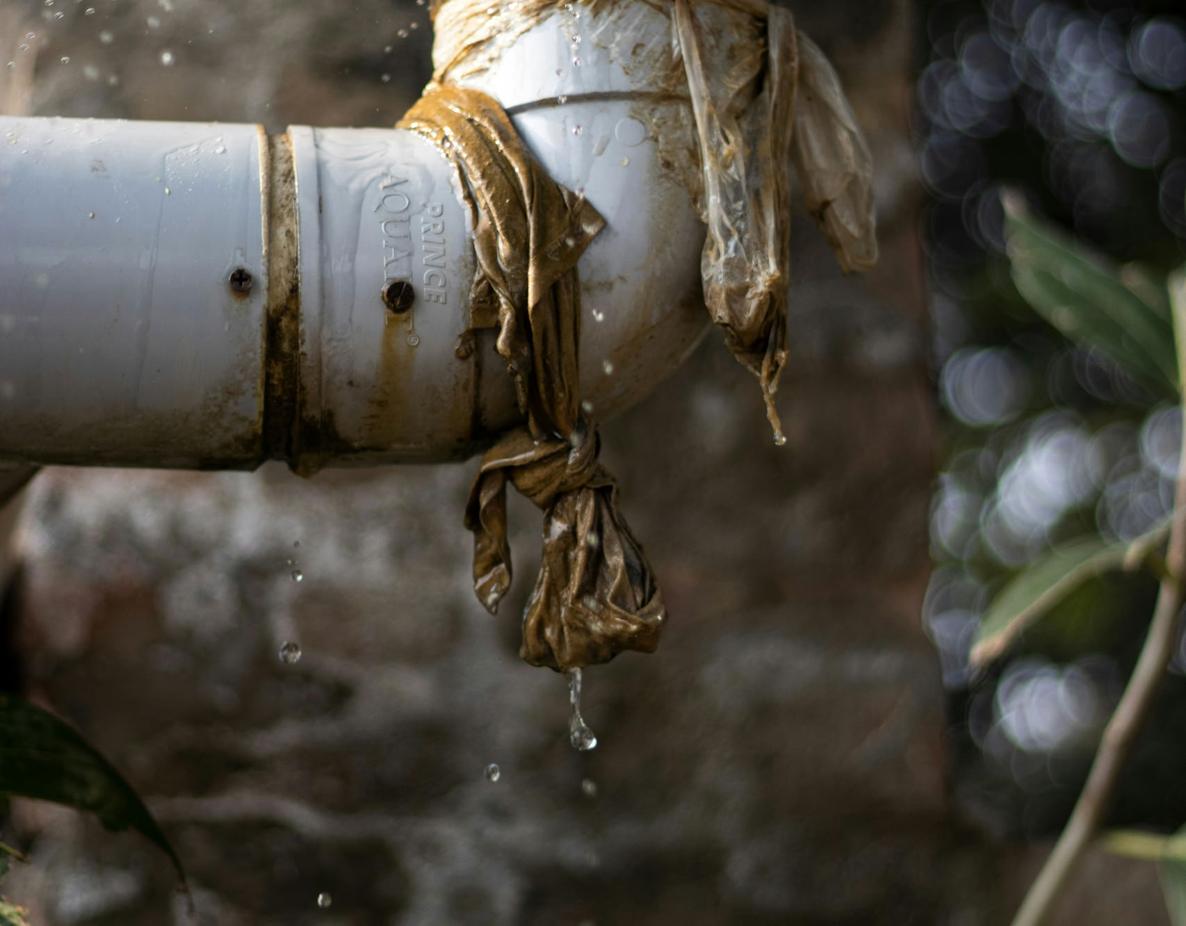 Close-up of a leaking plastic pipe outdoors with water dripping, showing wear and tear.